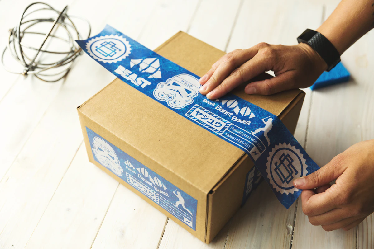 Seseorang memegang kardus paket yang sudah dilakban di atas meja packing
