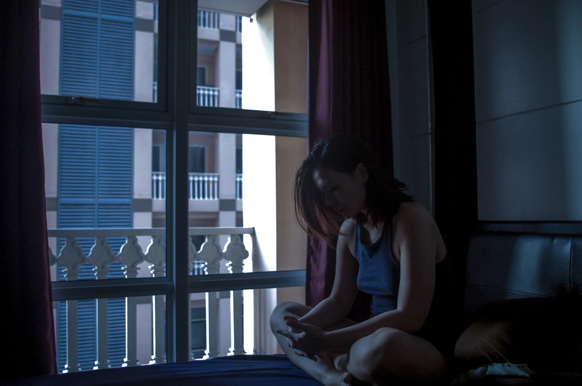 Seseorang duduk di tempat tidur dalam kamar gelap, wajahnya tersinari layar ponsel